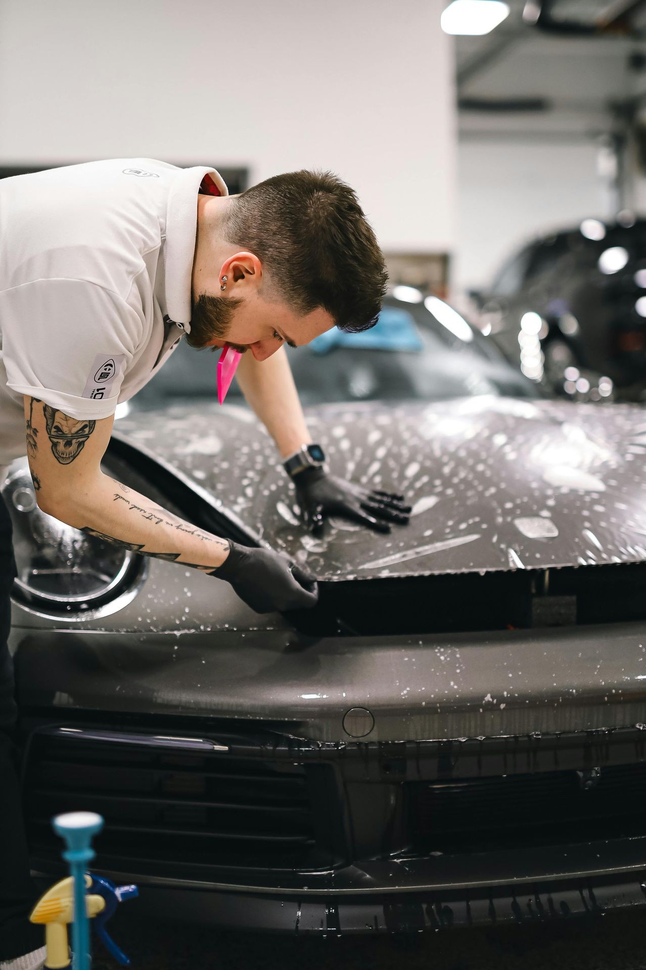 Person applying protective film to a wet car hood in a garage, focused on detail work.